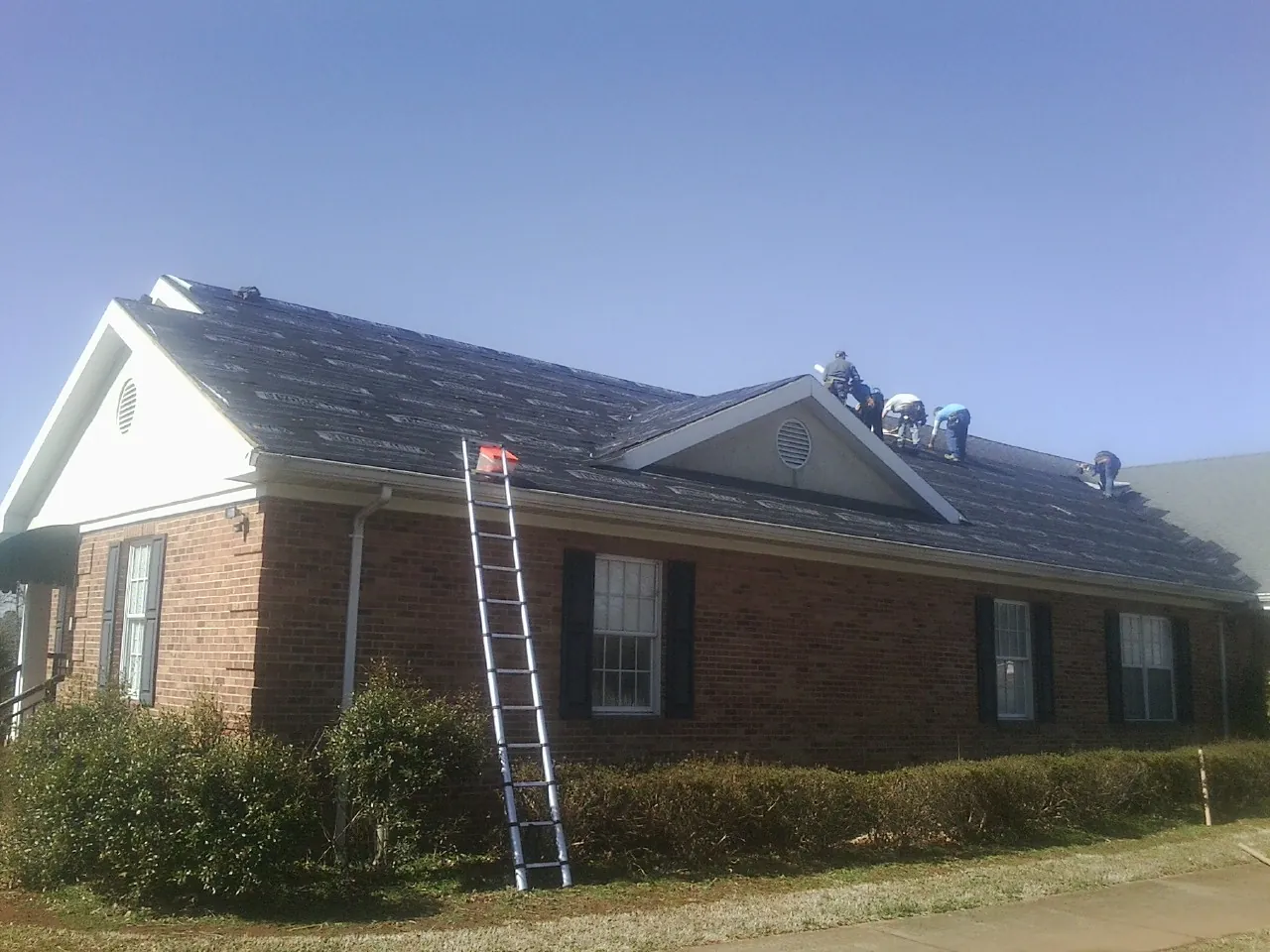 Crew tearing shingles off a brick ranch roof with a ladder set — Metal Roof Repair work by our crew in Bozrah