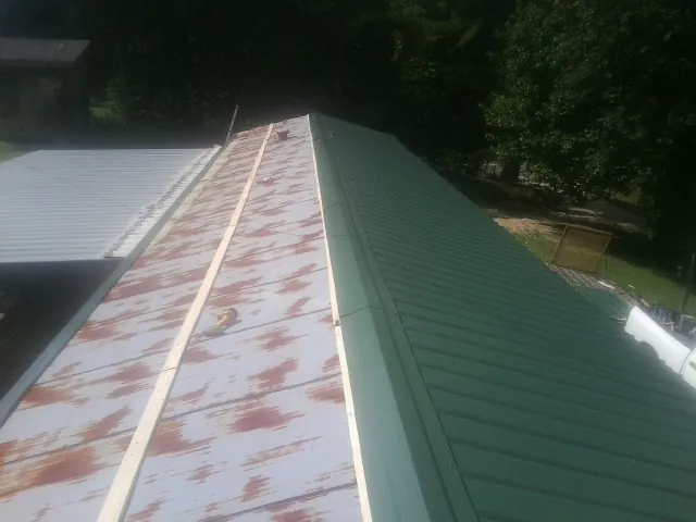 Old rusted panels beside newly installed green metal roofing — Wind Damage Roof Repair by Roofing Brothers in Bozrah