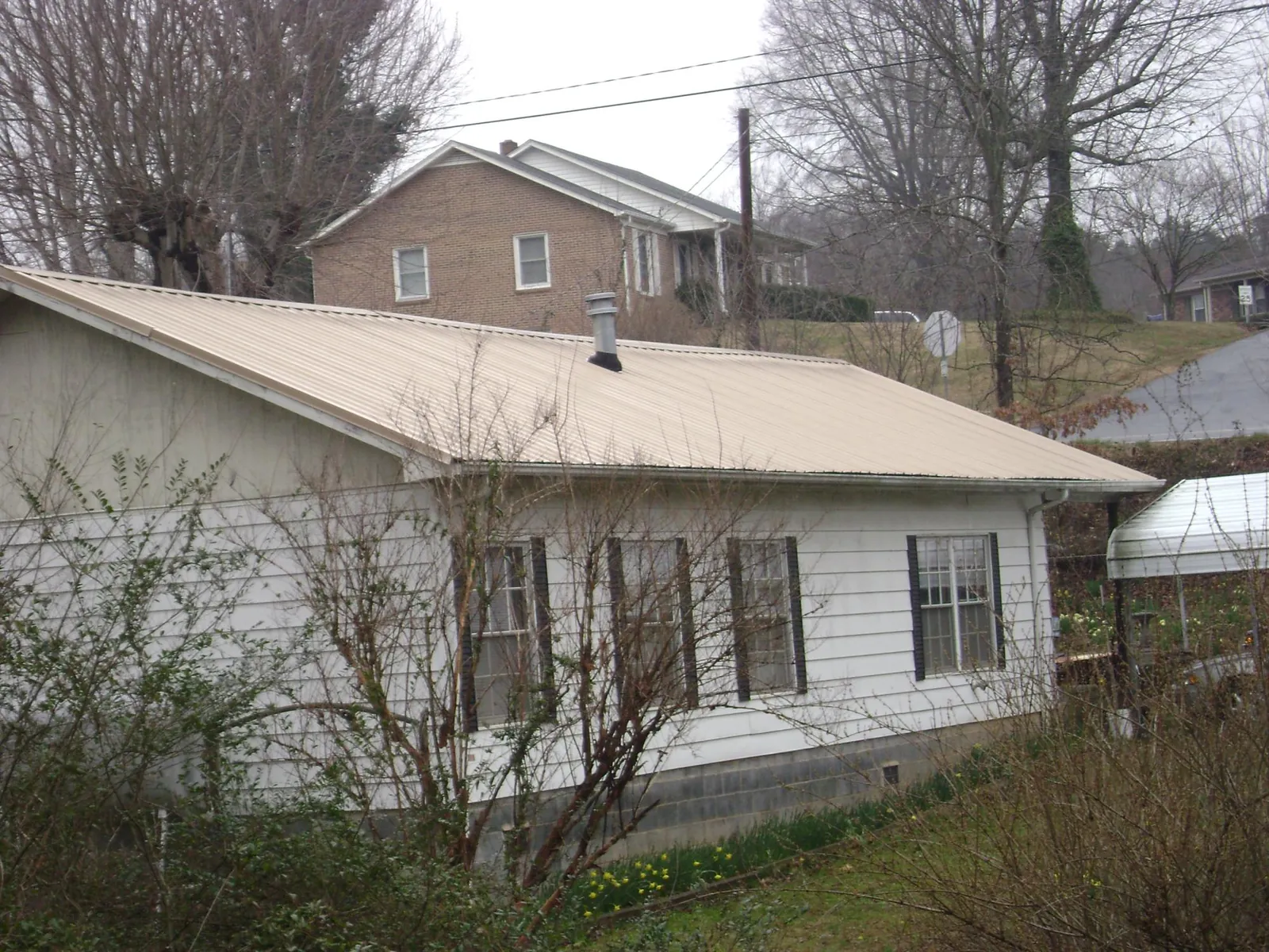 Tan metal roof on a white sided house set into a hillside — Commercial Roofing by Roofing Brothers in Bozrah